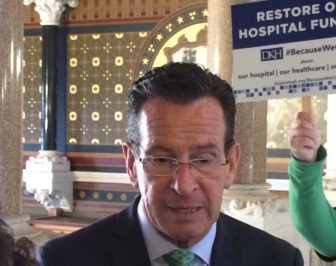 Gov. Dannel P. Malloy speaks to reporters as advocates argue to shield hospitals from budget cuts.