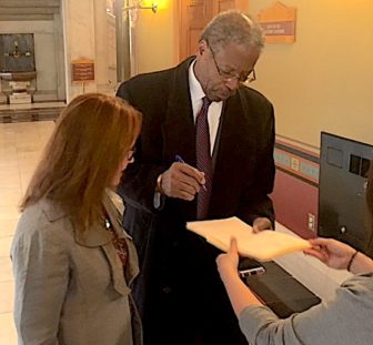 Sen. Eric Coleman signs a resignation as Secretary of the State Denise Merrill watches.